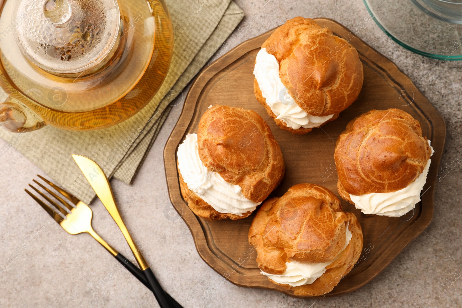 Photo of Delicious profiteroles filled with cream and tea on grey table, flat lay