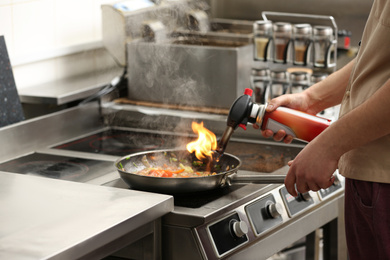 Photo of Male chef with manual gas burner cooking tasty food on stove in restaurant kitchen, closeup of hands