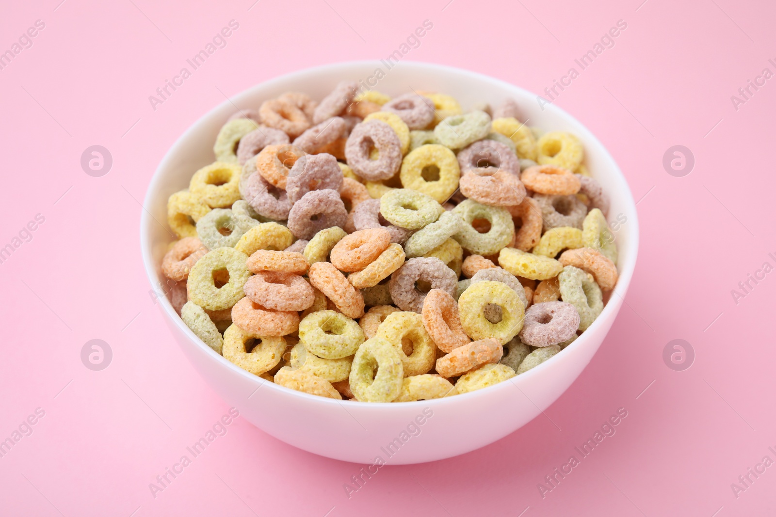 Photo of Tasty cereal rings in bowl on pink table, closeup