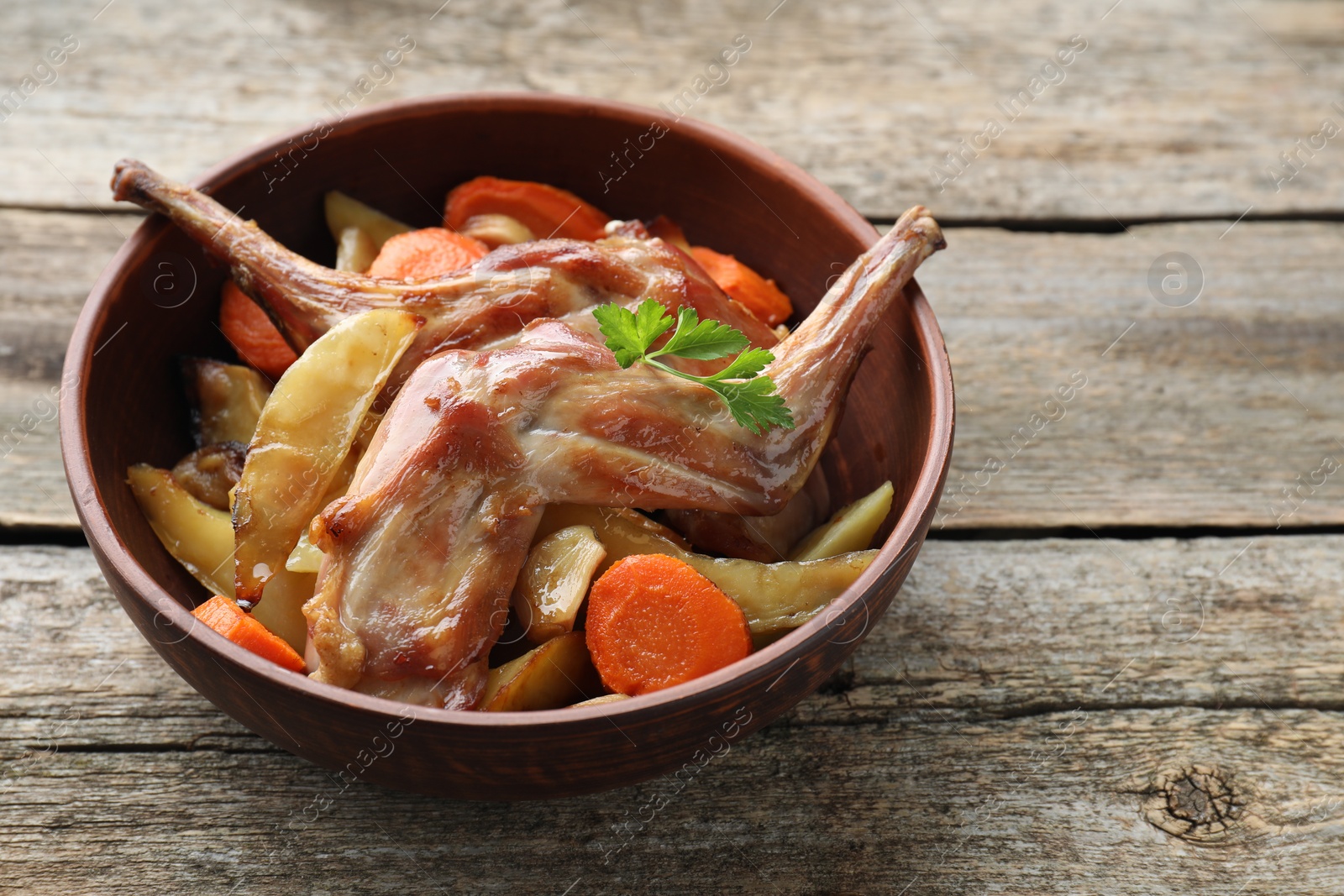 Photo of Tasty cooked rabbit with vegetables in bowl on wooden table, space for text