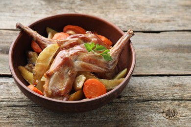 Photo of Tasty cooked rabbit with vegetables in bowl on wooden table, space for text