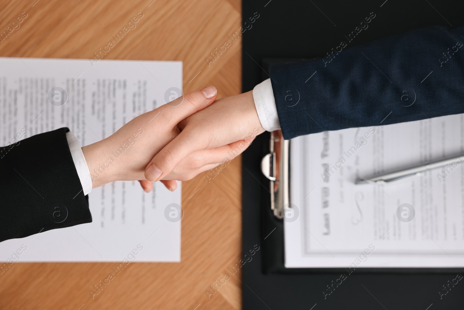 Photo of Notary shaking hands with client at wooden table, top view