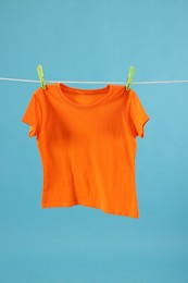 One orange t-shirt drying on washing line against light blue background