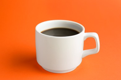 Photo of White mug of freshly brewed hot coffee on orange background