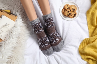 Photo of Woman wearing knitted socks on white fabric, top view. Warm clothes