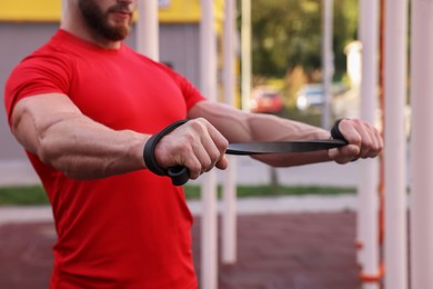 Photo of Muscular man doing exercise with elastic resistance band outdoors, closeup