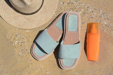 Photo of Stylish slippers, straw hat and bottle of sunblock on sand, flat lay. Beach accessories