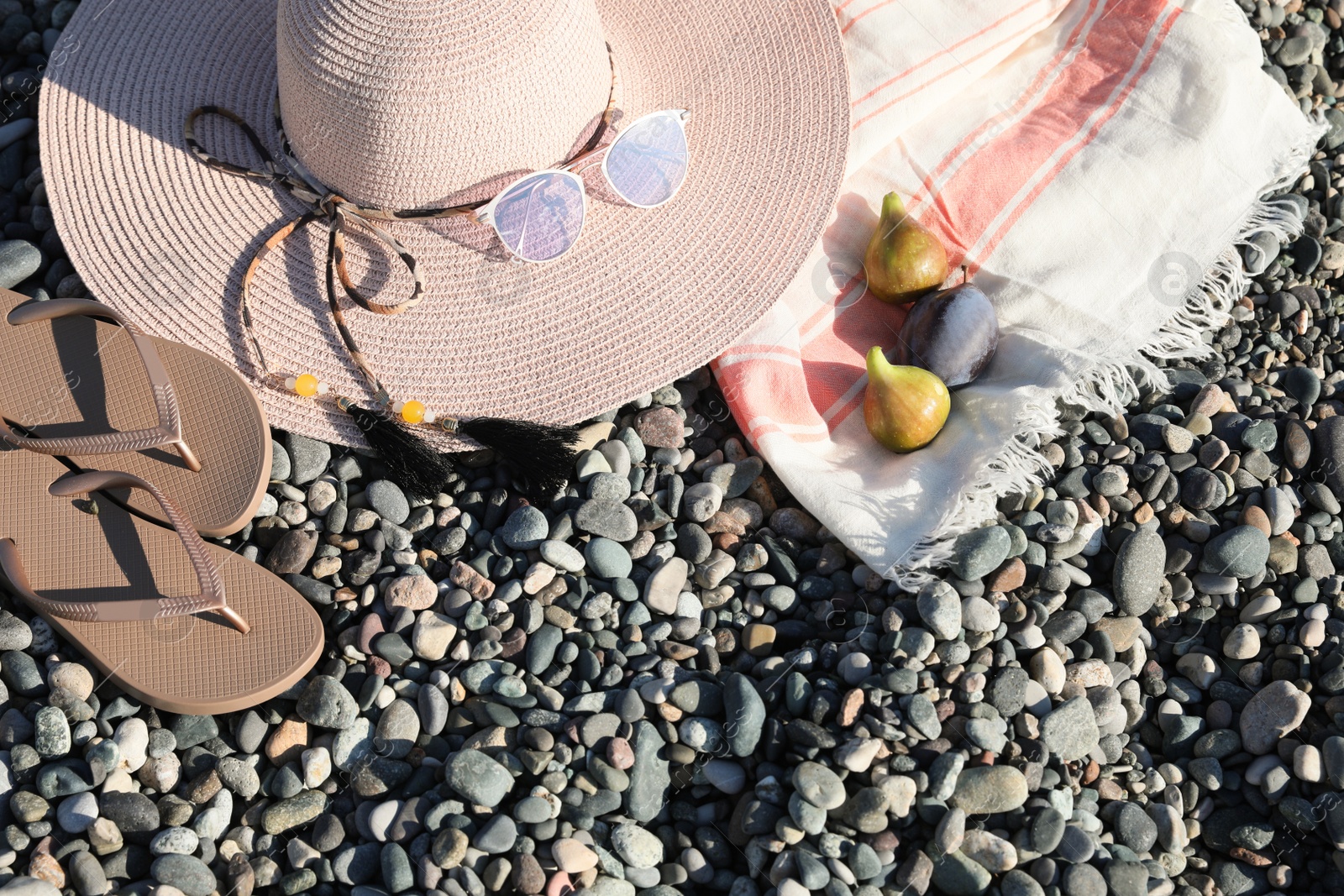 Photo of Beautiful hat with sunglasses and flip flops on pebbles, flat lay. Space for text