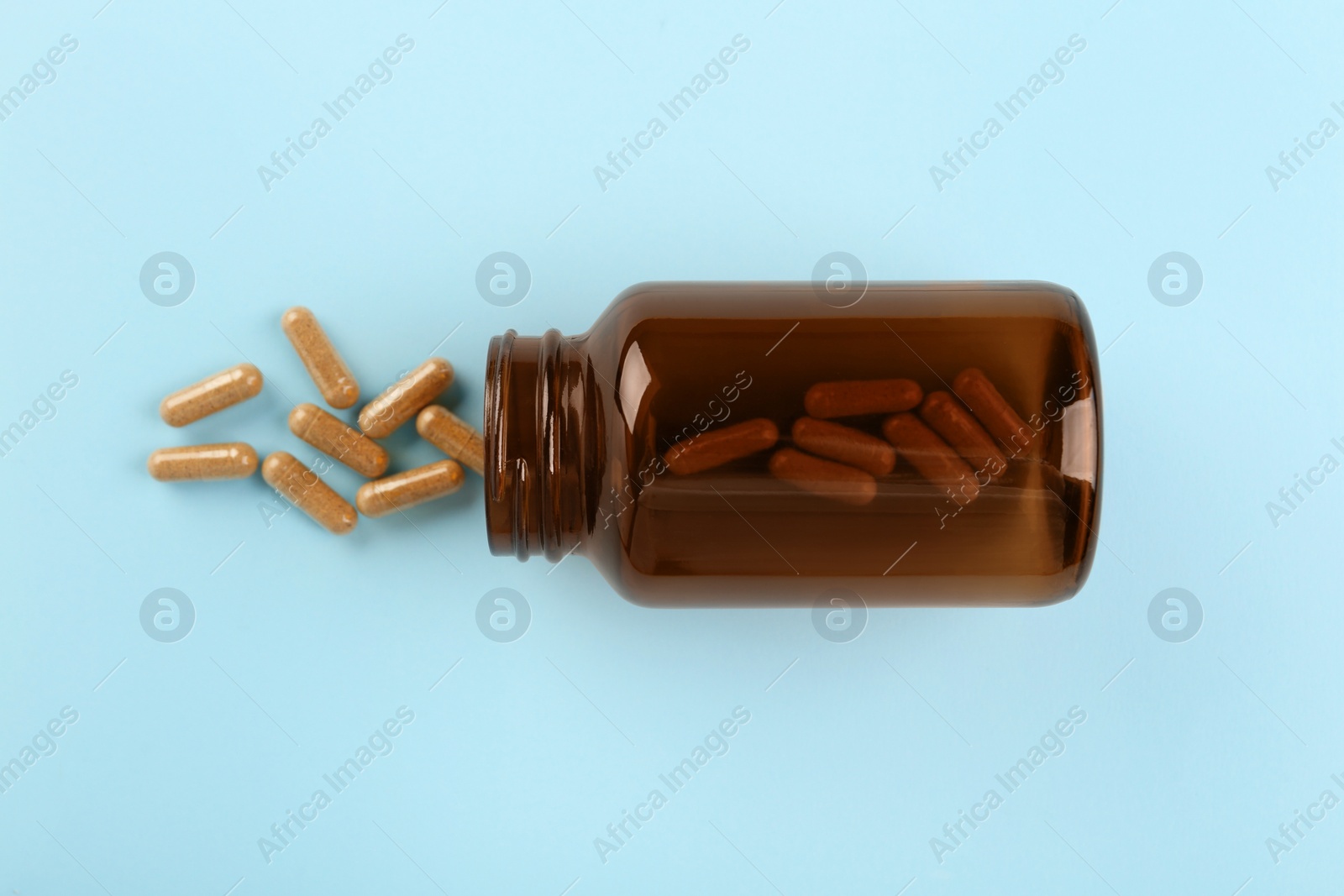 Photo of Bottle and vitamin capsules on light blue background, top view