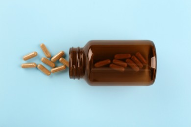 Photo of Bottle and vitamin capsules on light blue background, top view