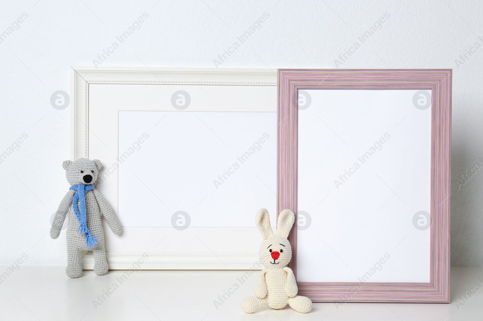 Photo of Soft toys and photo frames on table against white background, space for text. Child room interior