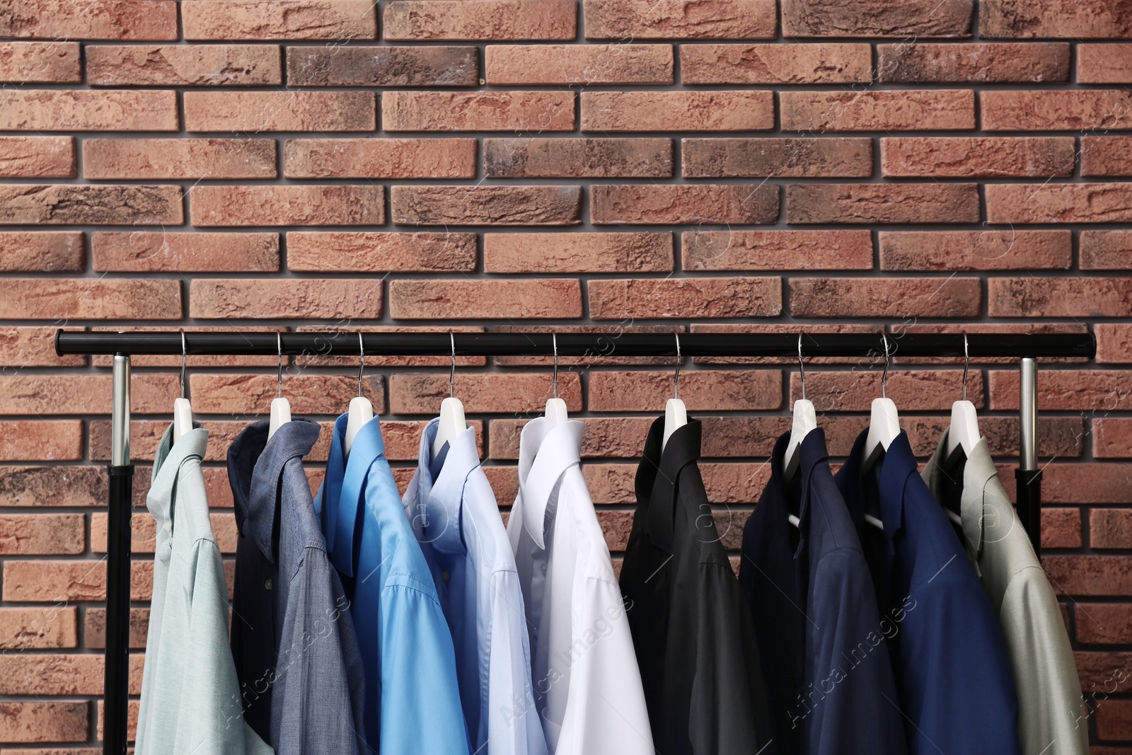 Photo of Wardrobe rack with stylish clothes near brick wall