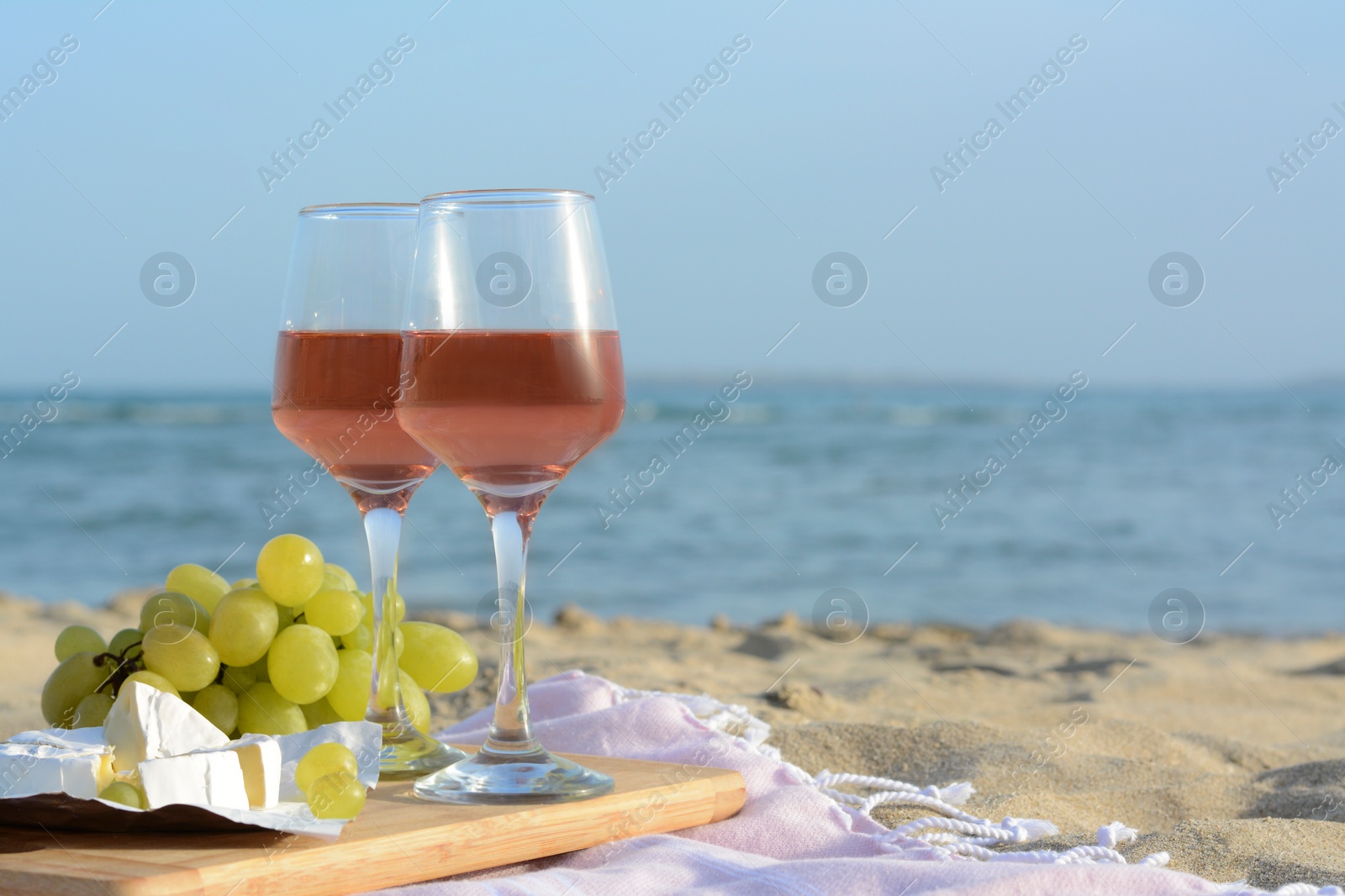 Photo of Glasses with rose wine and snacks on sandy seashore. Space for text