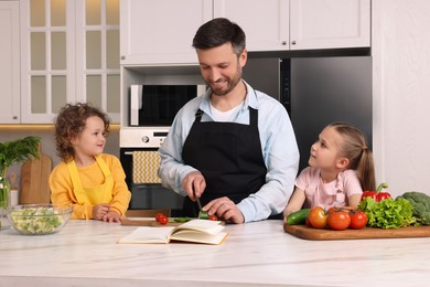 Photo of Happy man with his daughters cooking by recipe book in kitchen