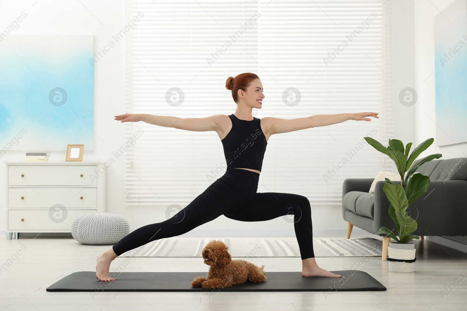 Photo of Happy young woman practicing yoga on mat with her cute dog at home