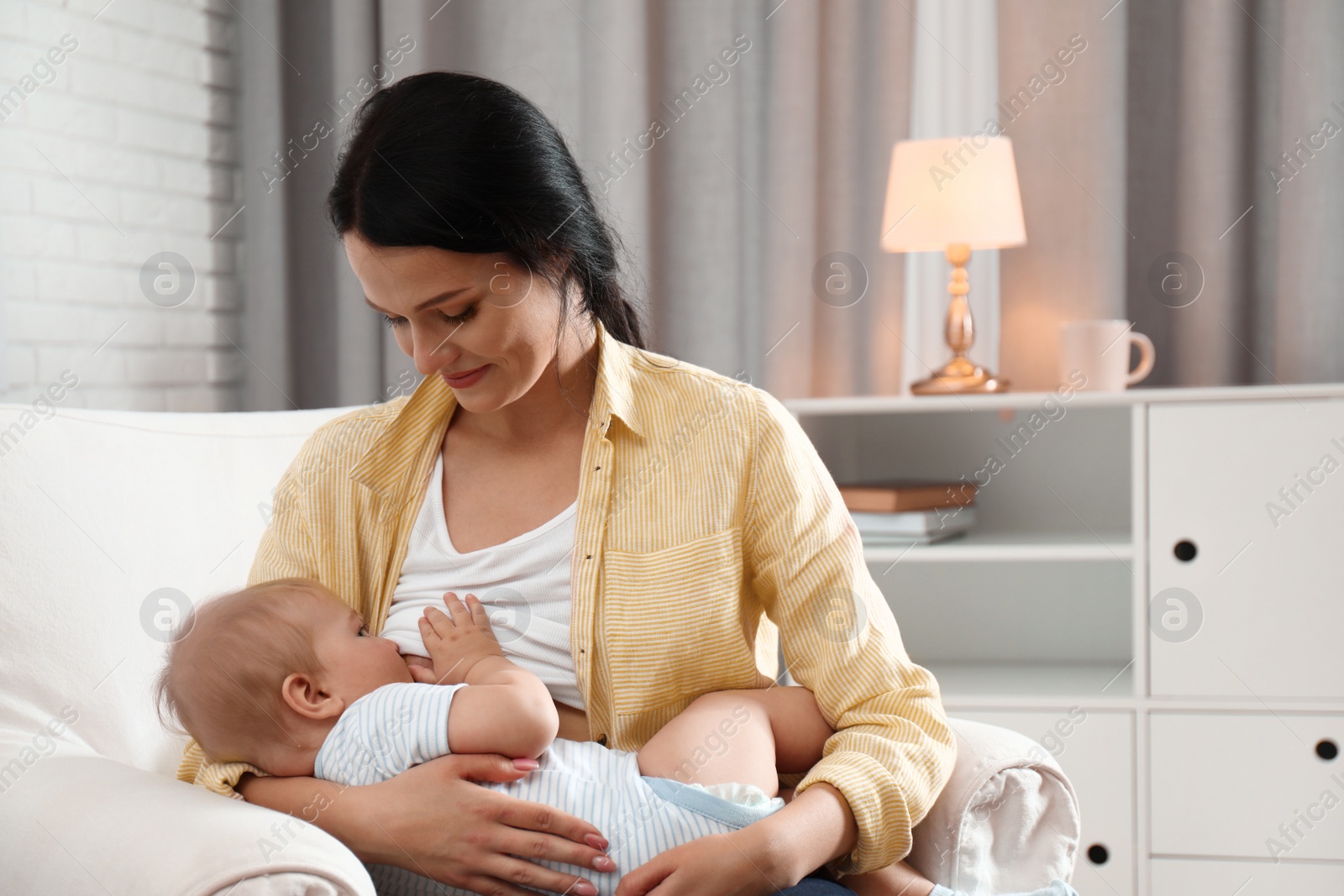 Photo of Woman breast feeding her baby in armchair at home