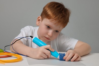 Photo of Boy drawing with stylish 3D pen at white table, selective focus