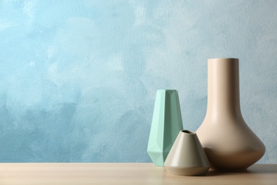 Stylish ceramic vases on wooden table against light blue background. Space for text