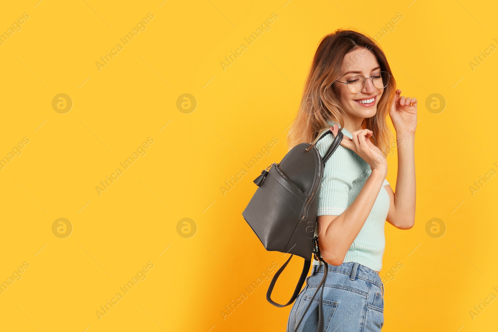 Photo of Happy woman with backpack on yellow background. Space for text