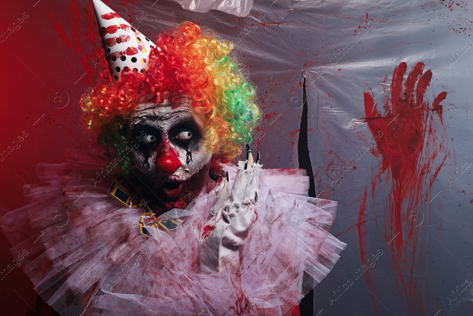 Photo of Terrifying clown near bloodstained plastic film. Halloween party costume