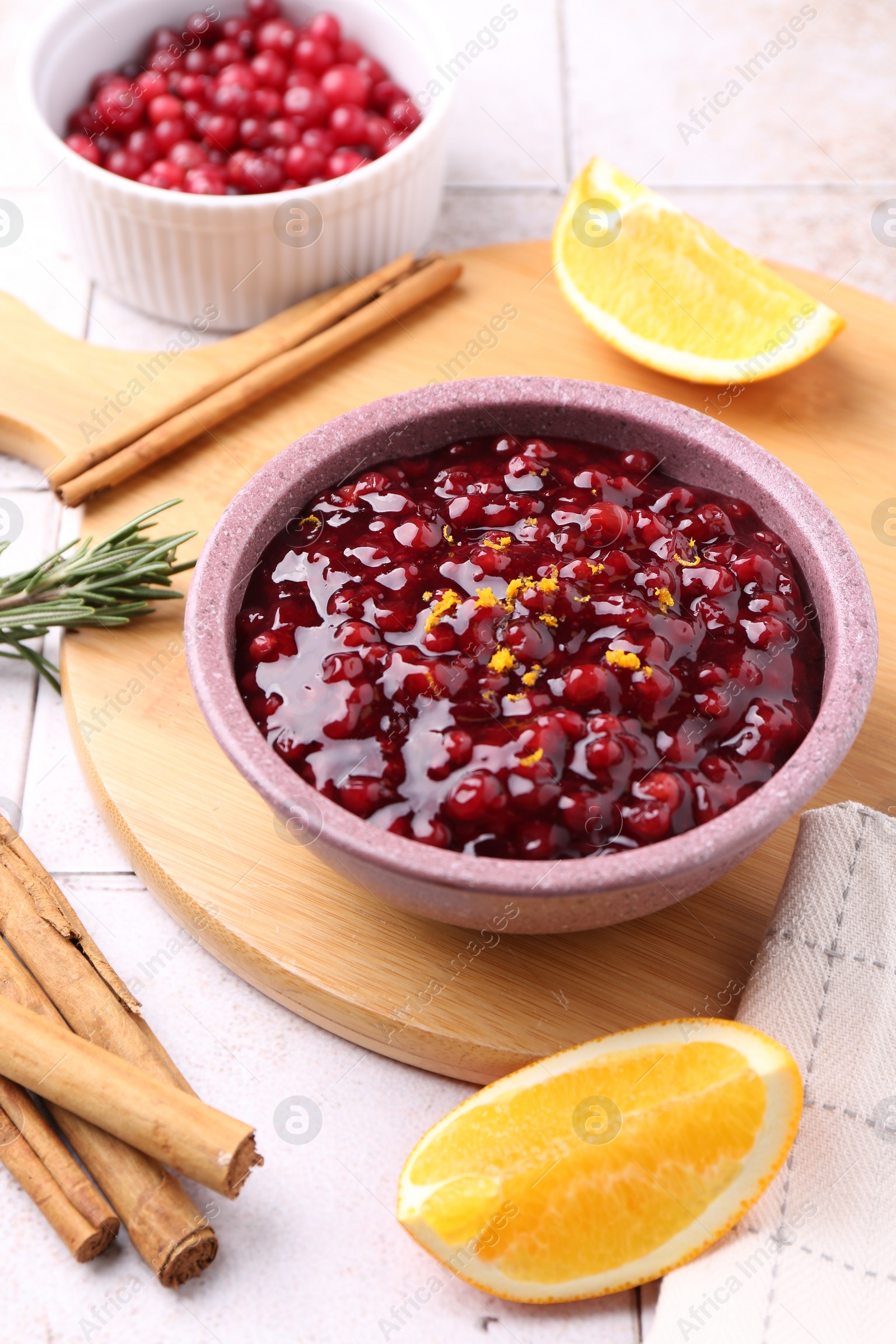 Photo of Tasty cranberry sauce in bowl and ingredients on white tiled table