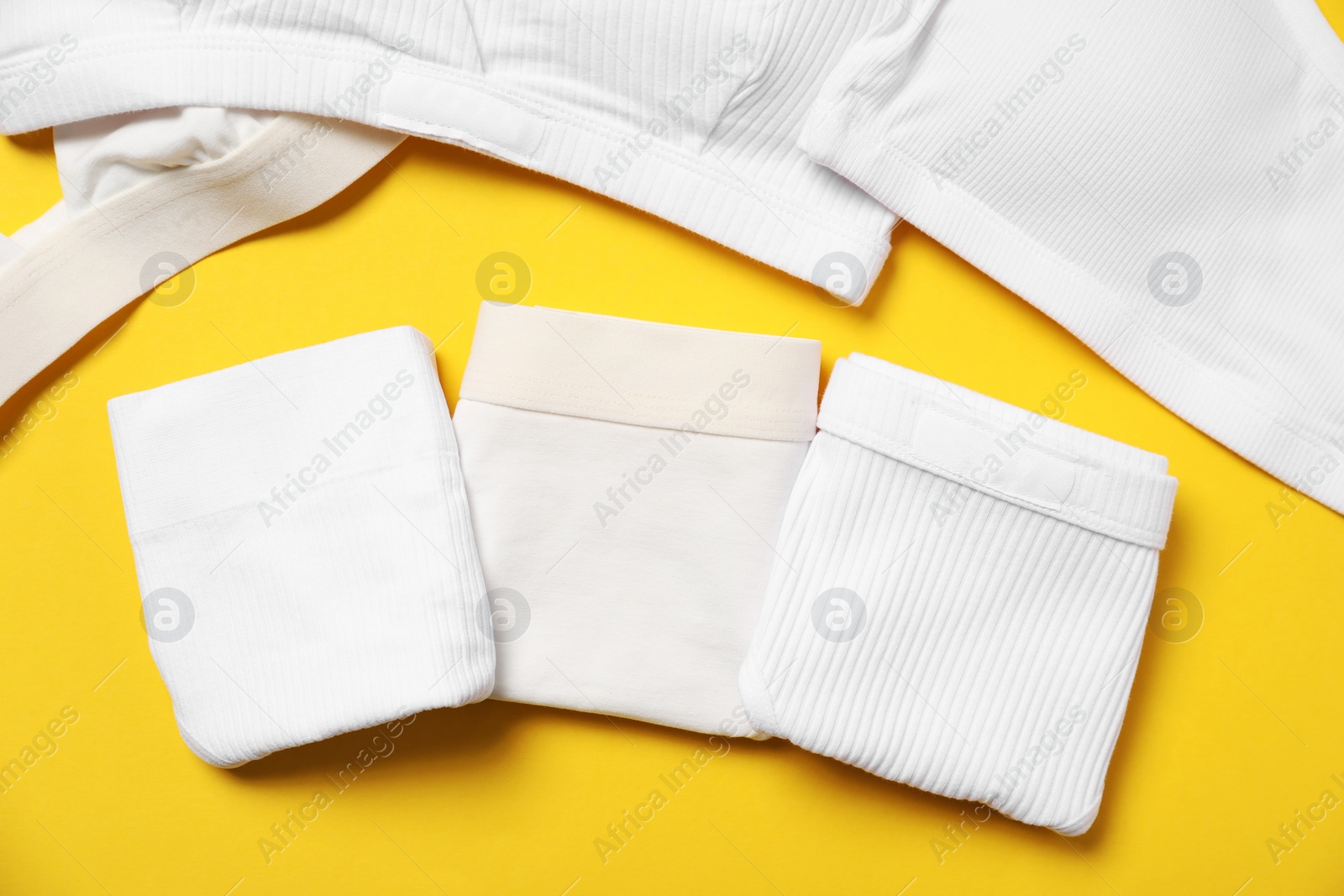 Photo of Stylish folded women's underwear on yellow background, flat lay