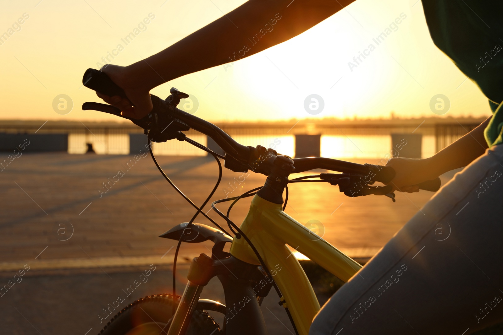 Photo of Young woman with bicycle on city waterfront at sunset, closeup