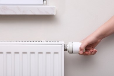 Photo of Girl adjusting heating radiator thermostat near white wall indoors, closeup