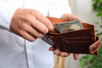 Man putting dollar banknote into wallet indoors, closeup. Money savings