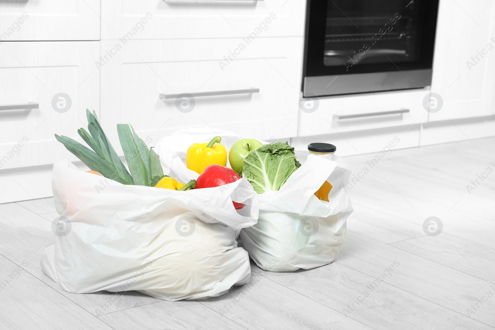 Photo of Plastic shopping bags full of vegetables and juice on floor in kitchen. Space for text