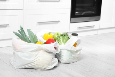 Plastic shopping bags full of vegetables and juice on floor in kitchen. Space for text
