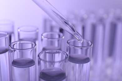 Photo of Dripping liquid from pipette into test tube on violet background, closeup