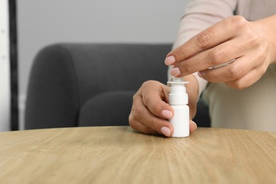 Woman opening nasal spray at wooden table indoors, closeup. Space for text