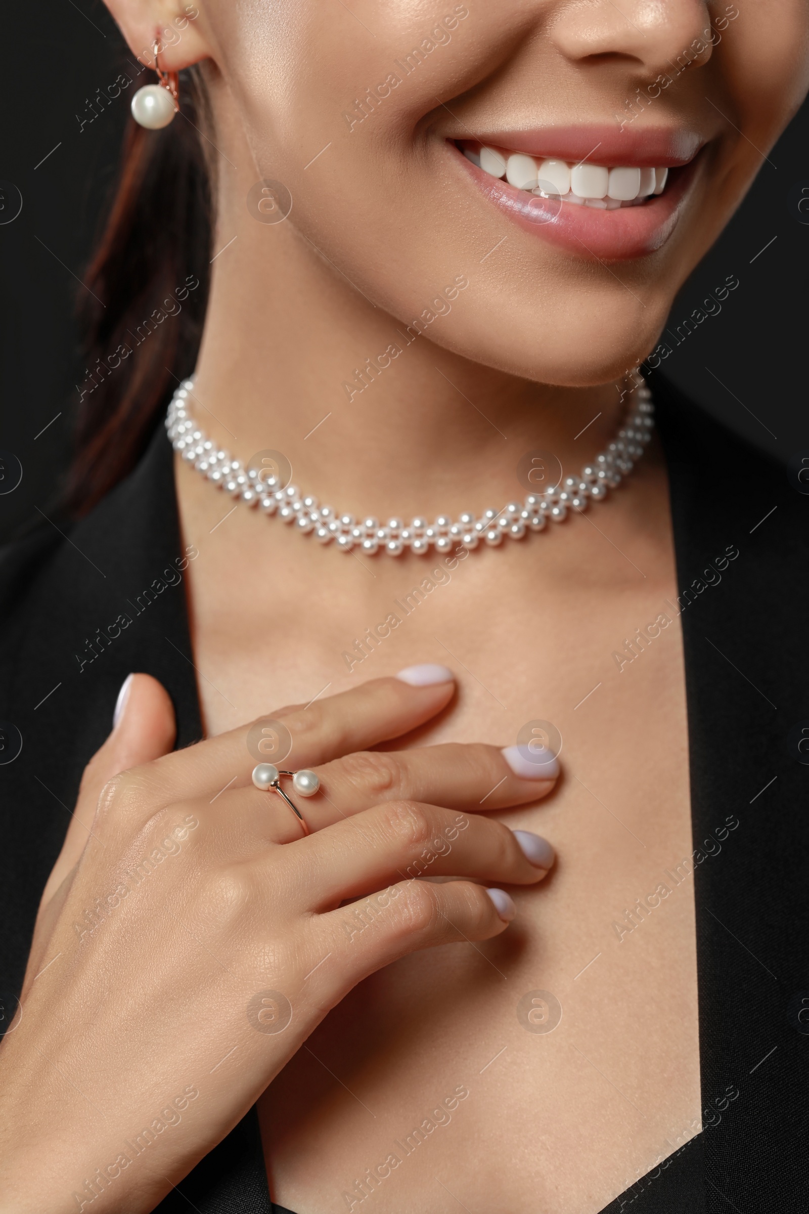 Photo of Young woman with elegant pearl jewelry on black background, closeup