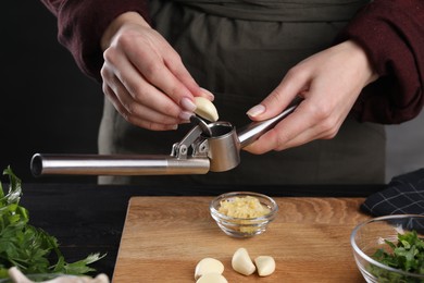 Photo of Woman squeezing garlic with press at black table, closeup