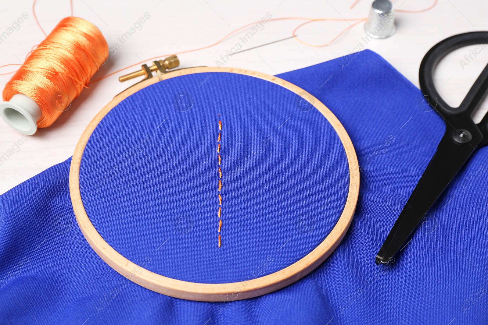 Photo of Blue cloth with stitches, sewing thread, needle and scissors on light table, closeup