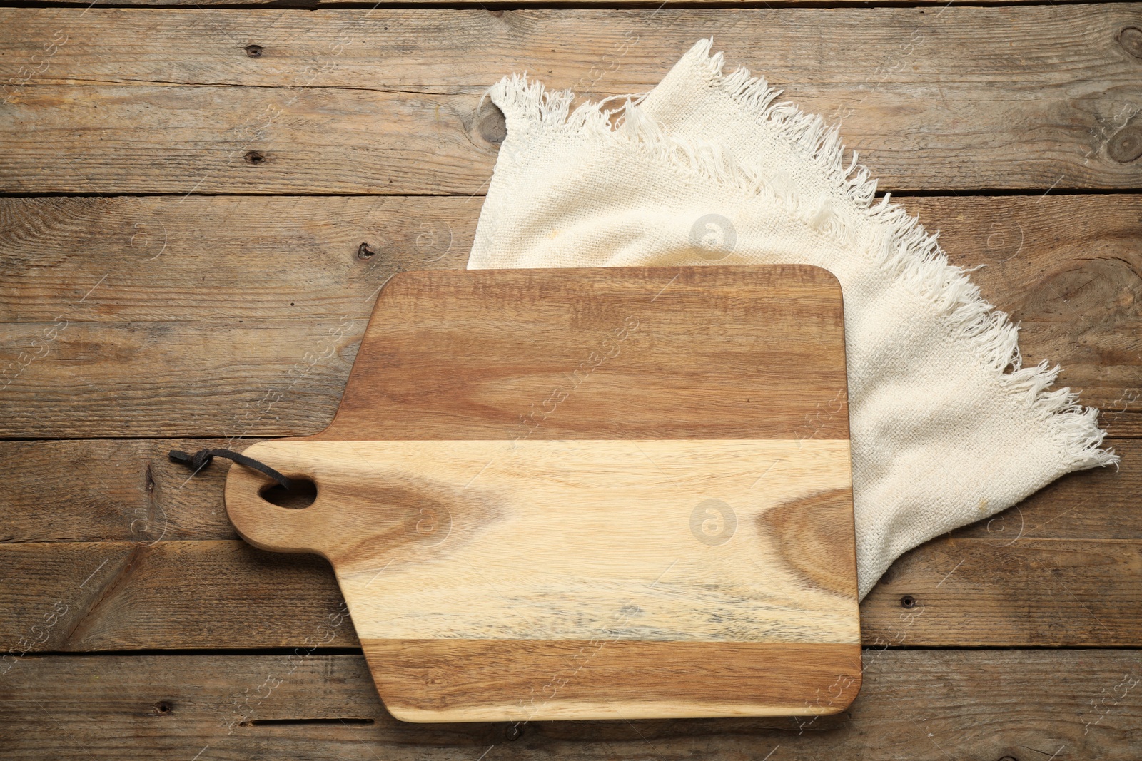 Photo of Cutting board and kitchen towel on wooden table, flat lay. Cooking utensil