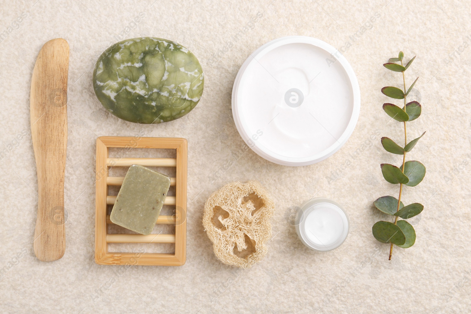 Photo of Flat lay composition with moisturizing cream in open jar and other body care products on light textured table