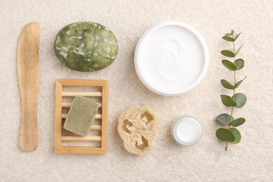 Photo of Flat lay composition with moisturizing cream in open jar and other body care products on light textured table