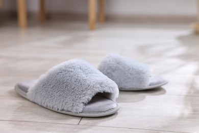 Grey soft slippers on light wooden floor at home, closeup