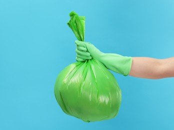 Photo of Woman holding plastic bag full of garbage on light blue background, closeup. Space for text