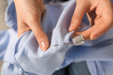 Photo of Woman sewing on light blue fabric with thimble and needle, closeup