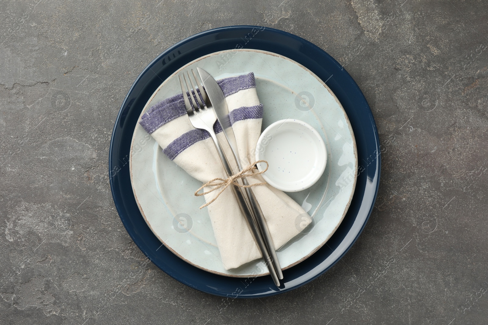 Photo of Stylish setting with cutlery, plates, bowl and napkin on grey textured table, top view