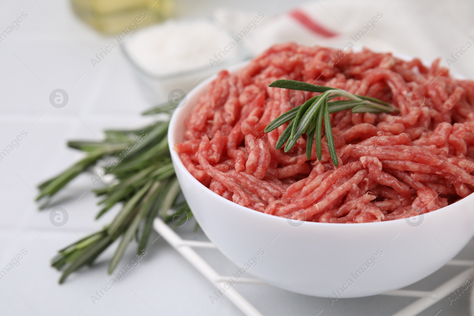 Photo of Fresh raw ground meat and rosemary in bowl on light table, closeup. Space for text