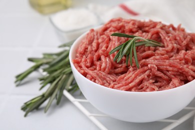 Fresh raw ground meat and rosemary in bowl on light table, closeup. Space for text