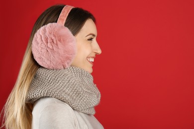 Photo of Happy woman wearing warm earmuffs on red background, space for text
