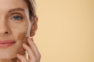 Woman with swatches of foundation on face against beige background, closeup. Space for text