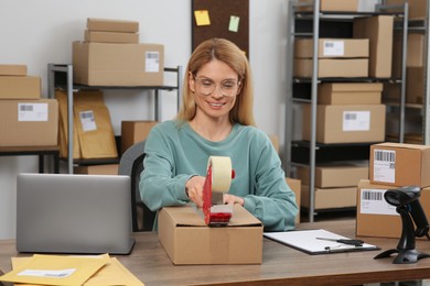 Photo of Seller taping parcel at table in office. Online store
