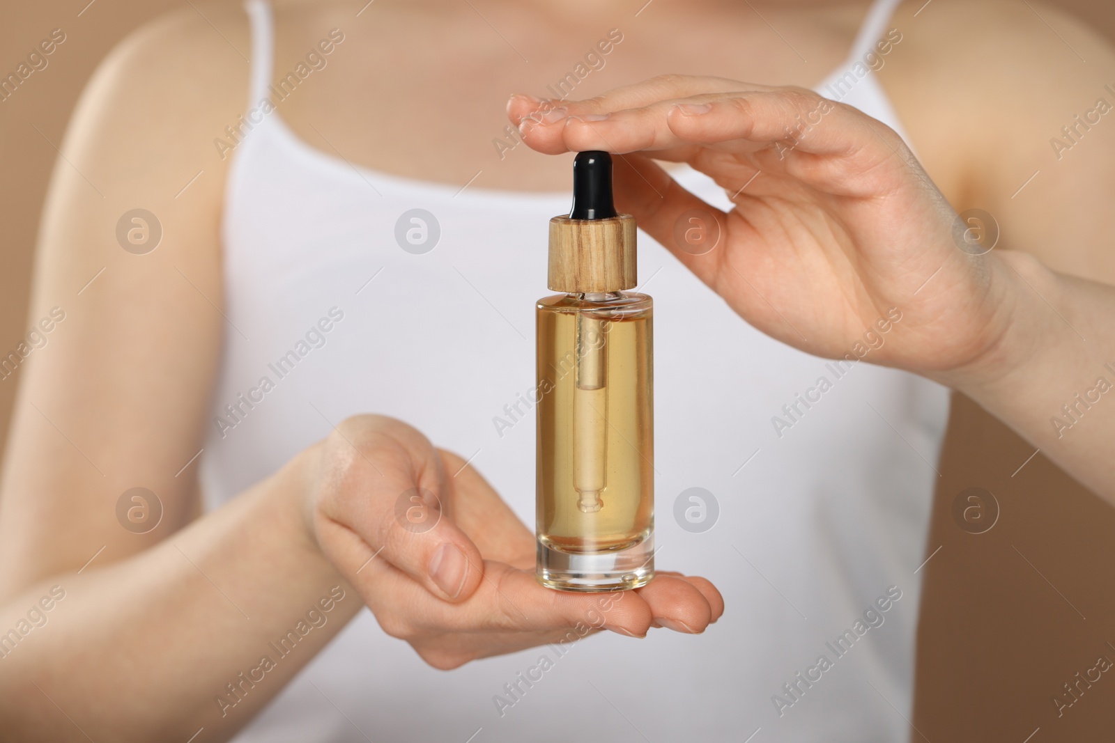 Photo of Woman holding bottle of essential oil on brown background, closeup