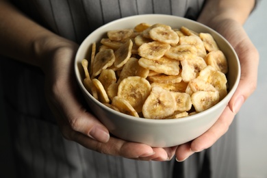 Photo of Woman holding bowl with sweet banana slices on light background, closeup. Dried fruit as healthy snack